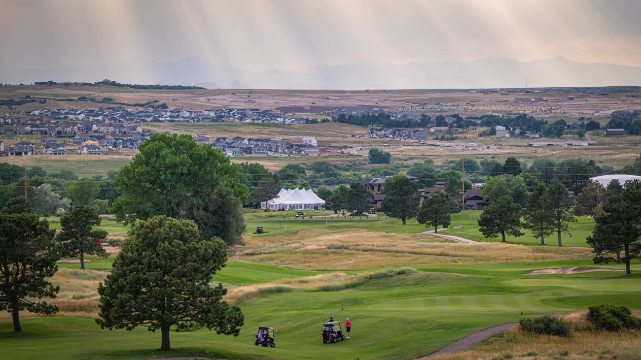 Prairie grass and mown fairway running west toward the mountains as shafts of light break through cloud.
