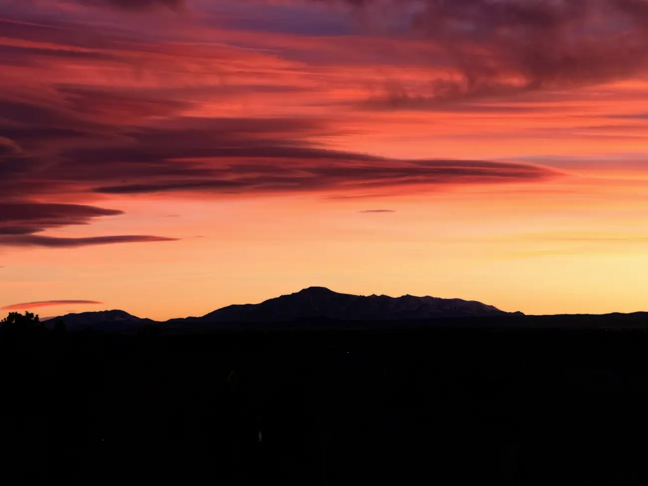 Lenticular cloud burning red and orange above the silhouette of Pikes Peak after sunset.